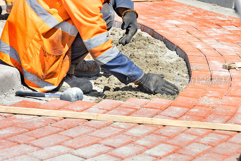一位泥瓦匠师傅在道路上的交通环岛周围铺设橙色的石板。
