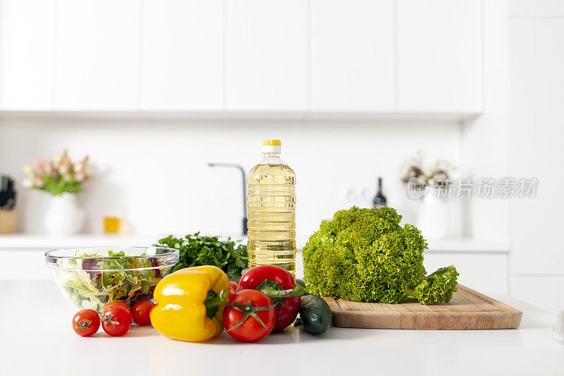 白色现代厨房的桌子上放着沙拉的配料，蔬菜、西红柿、辣椒和一瓶油
