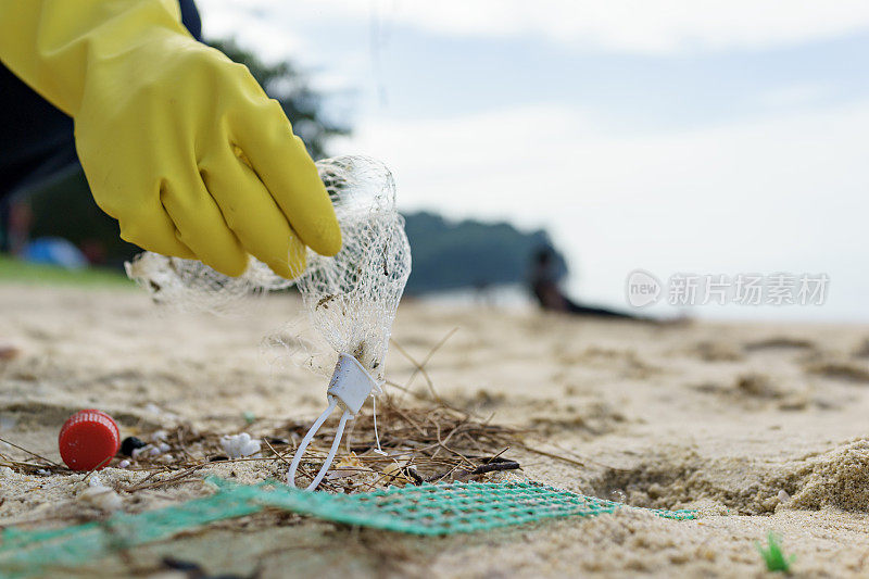 一名志愿者戴着手套捡拾海滩上被冲上岸的塑料污染的特写照片，突显了海洋环境中塑料污染的持续问题。