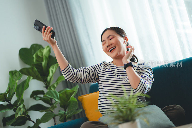 快乐的女人在家里用智能手机和耳机听音乐。