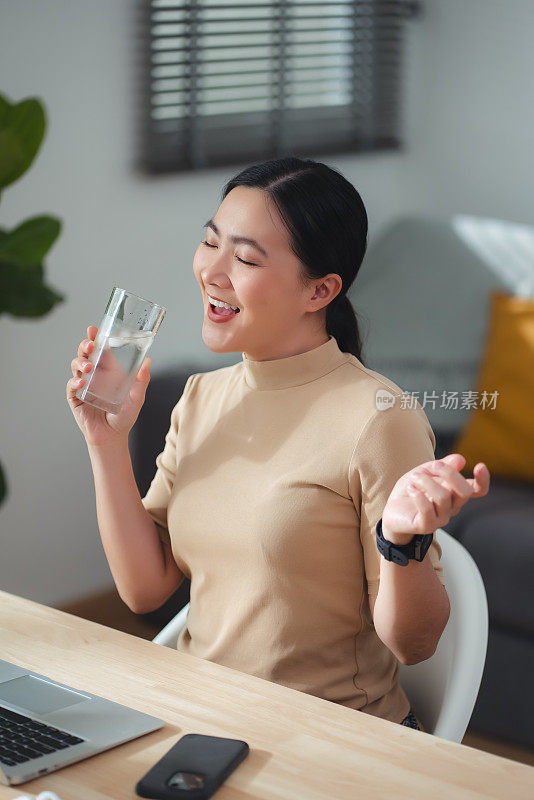 坐在家里办公室喝凉水休息的亚洲女性。