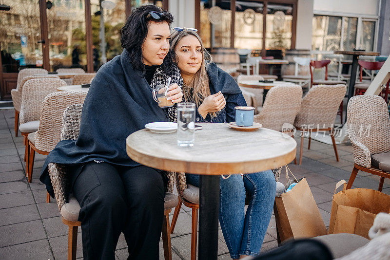 秋天，两个年轻女子坐在咖啡馆外面喝咖啡