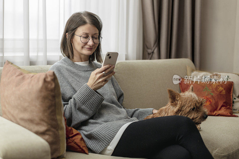 年轻的成年女子坐在客厅的沙发上玩手机