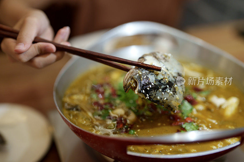 一个女人在餐馆里用筷子享用新鲜的水煮鱼配酸菜和辣椒的特写
