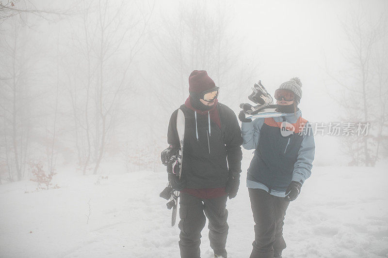 两个好朋友一边聊天，一边拿着滑雪板向山顶走去，准备滑雪