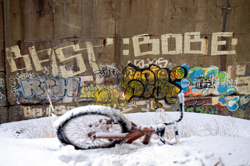 雪地里的自行车被遗弃在桥下，上面有涂鸦