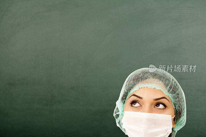 戴着医用口罩的女医生在黑板上思考