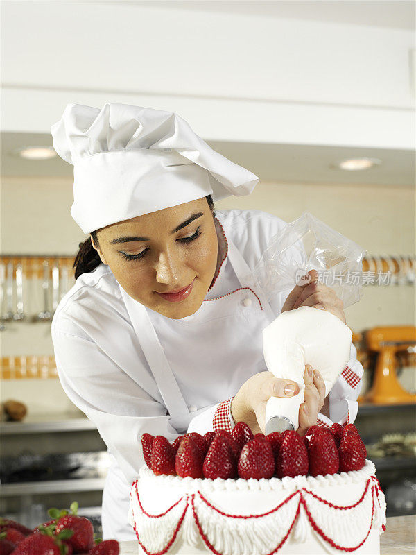 女面包师用整个草莓装饰一个大蛋糕