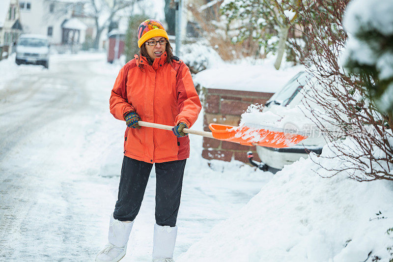 一个成熟的女人在清扫屋前的积雪