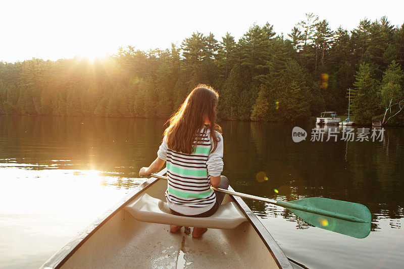 太阳升起时，女孩在湖中划着独木舟