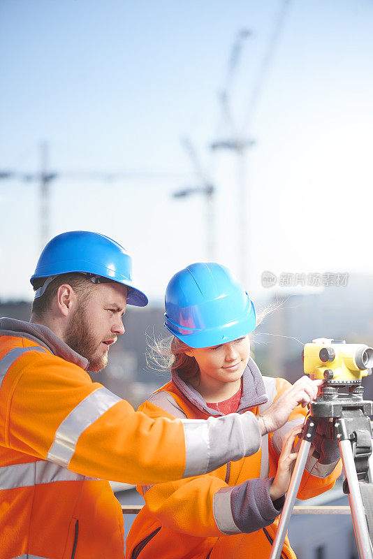 女性建筑工地测量师和她的主管使用经纬仪