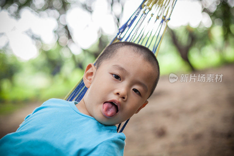 亚洲男孩躺在吊床上，伸出舌头