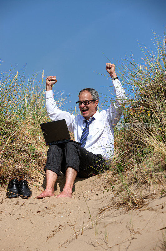 成熟的商人在沙滩上举起手提电脑