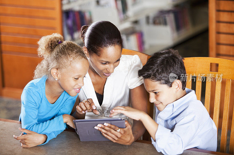 儿童与教师在图书馆使用数字平板电脑