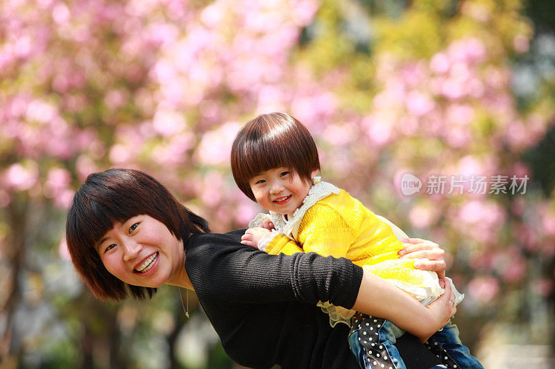 快乐的亚洲母亲背着女儿在春天的花园