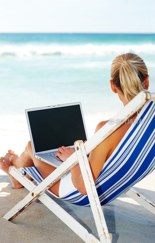 年轻女子一边用笔记本电脑工作，一边在海滩上休息