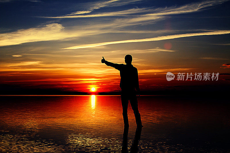 一个人站在日落前，在盐湖上竖起大拇指。