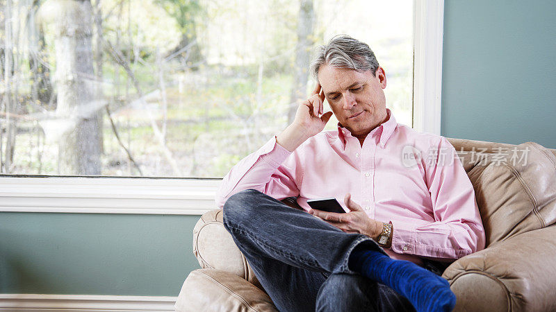 一名50多岁的男子坐在家里用智能手机，一脸关切