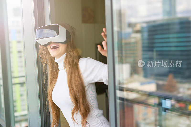 年轻漂亮的女人戴着虚拟现实眼镜在阳台上