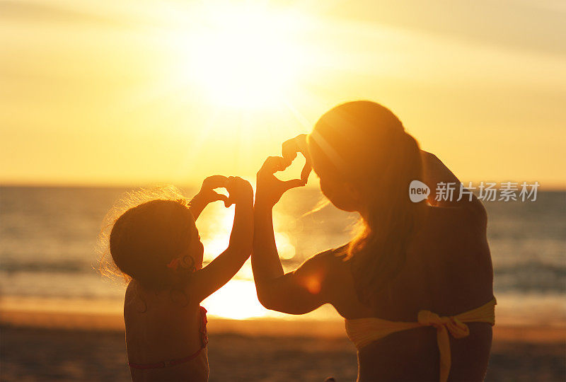 爱的概念，父母和幸福的家庭。母亲和孩子的女儿在日落时从手上露出心来