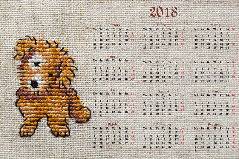 2018年英文日历。日历被画在一块织物上，上面绣着2018年的标志是一只狗。
