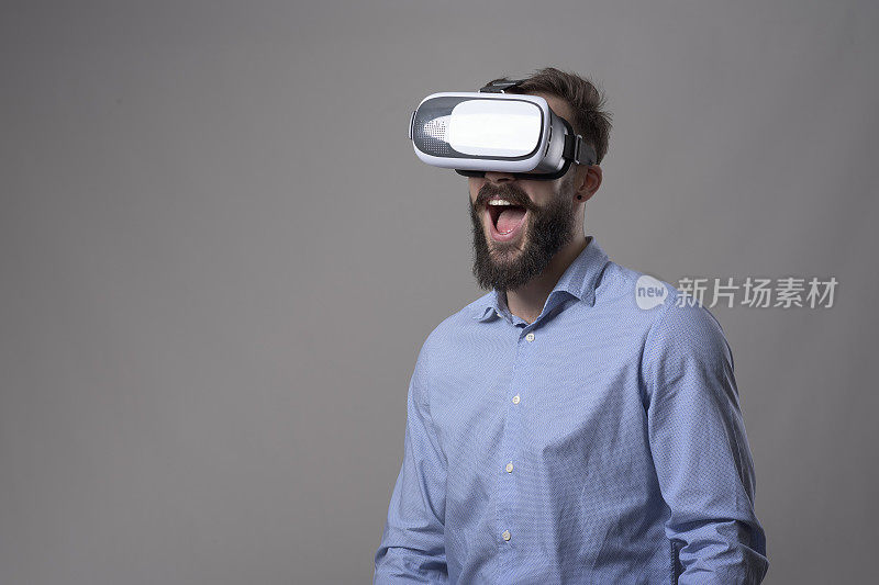 肖像的惊奇兴奋的年轻胡子男子看着虚拟现实眼镜与张着嘴的表情
