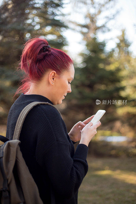 一个艳阳天在公园里用手机自拍的红发美女