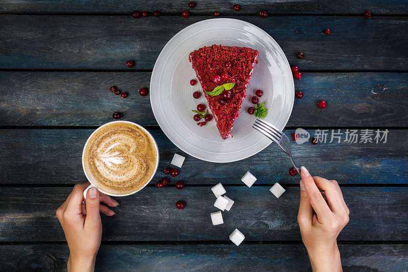 前视图。一块美味的红色天鹅绒蛋糕和拿铁咖啡，女人的手放在彩色的木制背景上