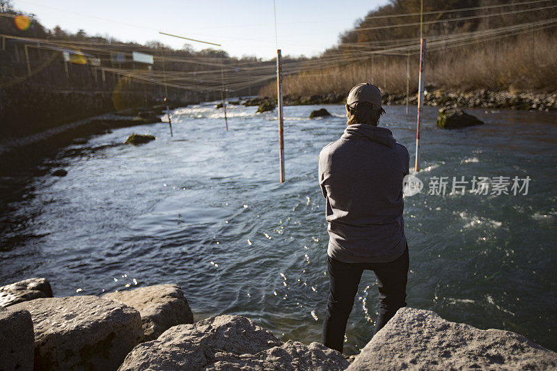 年轻的成年男子站在河岸上看皮划艇激流回旋赛道