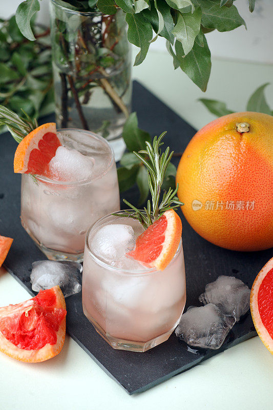 葡萄柚新鲜鸡尾酒与冰和迷迭香在玻璃上的黑石背景，夏季时间，度假村酒吧菜单特写