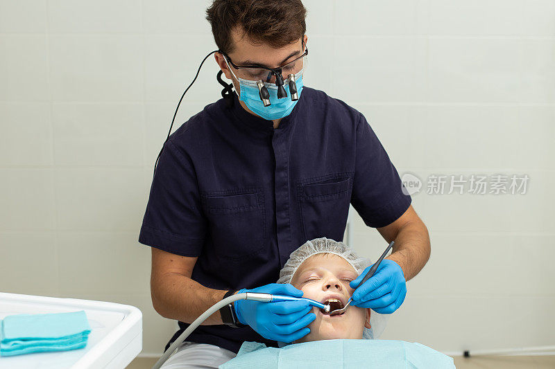 一个男孩戴着手套和显微镜眼镜，让口腔医生给他的牙齿钻孔