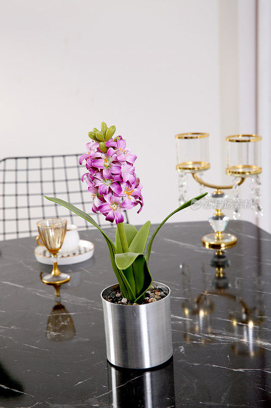在一个优雅的餐厅里，白色大理石桌上放着一个金色花瓶，里面放着淡紫色的花朵，米黄色的墙壁上镶着花边