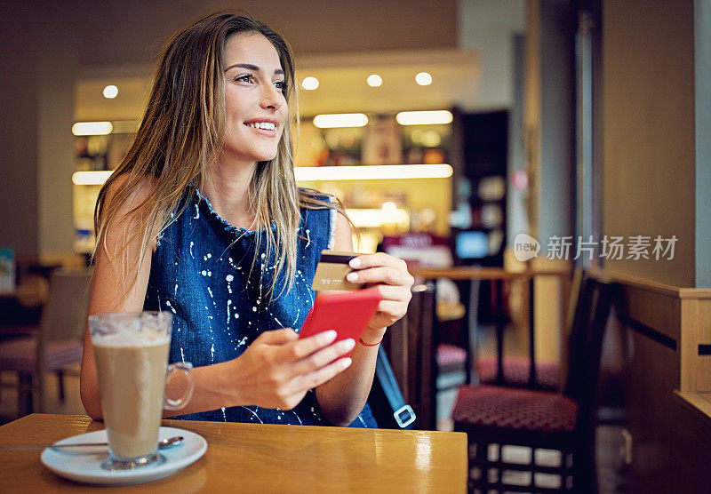 一个年轻的女孩坐在咖啡馆里，用她的信用卡在网上购物