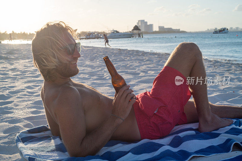 独自旅行度假的年轻人在海滩上喝啤酒，享受自由的日落