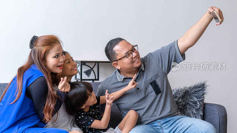 一位马来父亲在客厅用智能手机与家人自拍