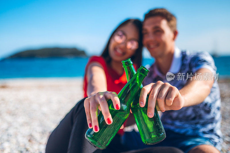 年轻夫妇在海滩上喝啤酒