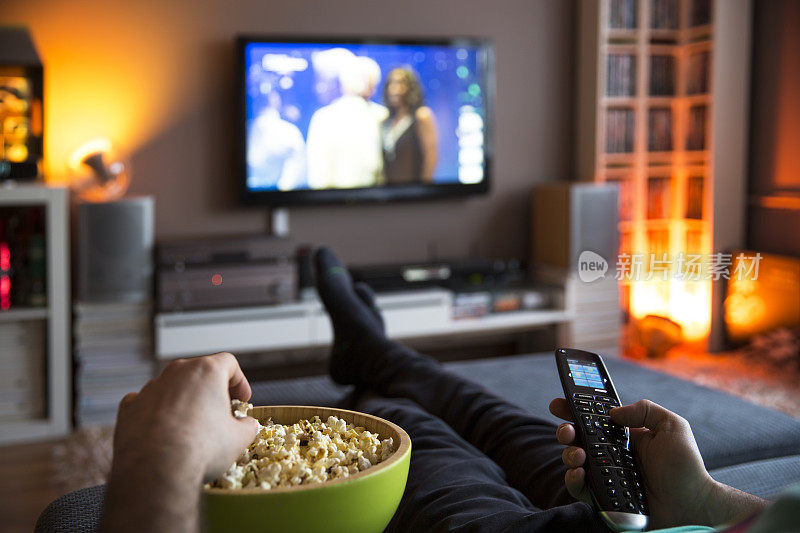 男人在家里放松看电视，吃爆米花和上网