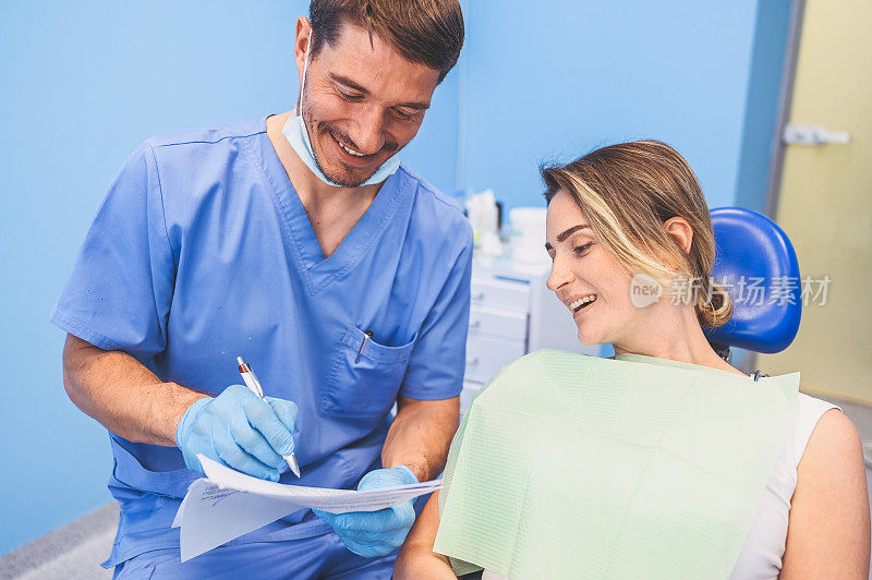 牙科医生在牙科诊所写结论和诊断。口腔医学与健康理念。年轻英俊的男医生戴着一次性医用口罩和手套与快乐的女人微笑。