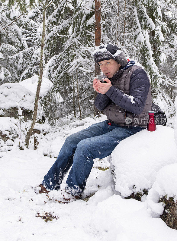 一个男人，一个白种人，正在冰天雪地的森林里喝热咖啡。