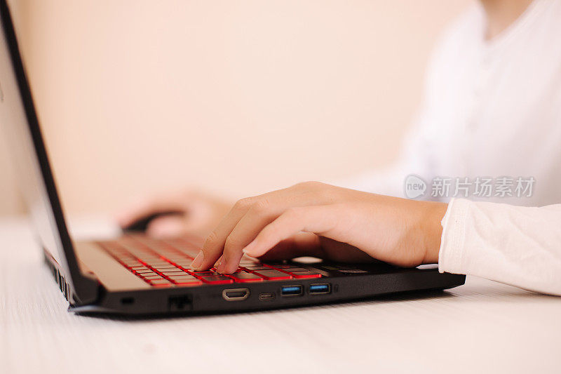 一个十几岁的男孩在白色的房间里玩电脑游戏。玩家在笔记本电脑的网络摄像头上捕捉视频。专注于手