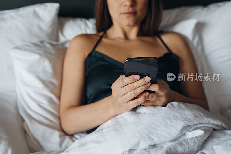 商界女性:躺在床上使用手机的匿名年轻女性