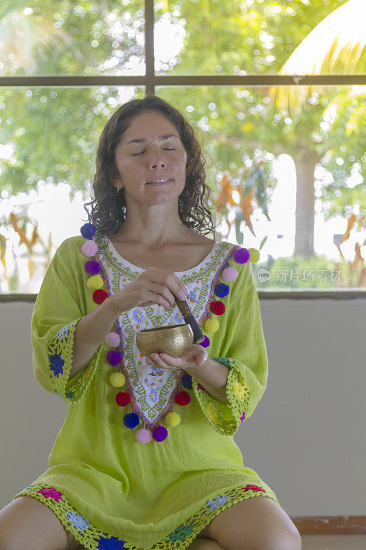 一个单身的运动中年年轻活跃的拉丁精神寻求者练习瑜伽和冥想，在西藏唱歌碗坐在一个工作室的瑜伽垫上，穿着一件绿色的印度衬衫。