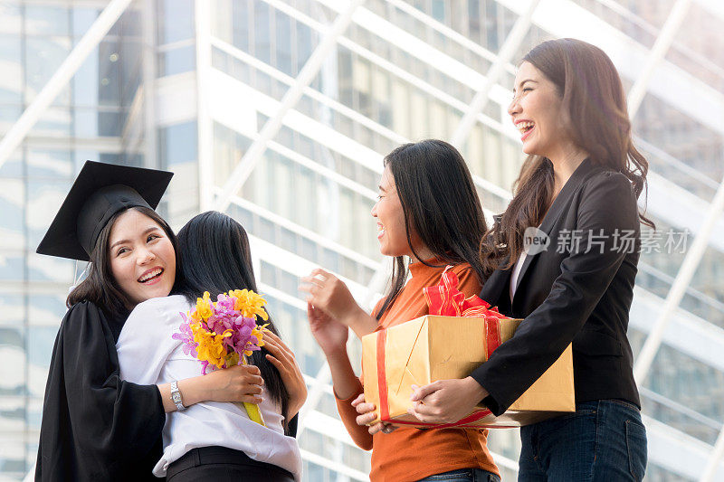 人们怀着快乐和感恩的心情，带着毕业礼服和毕业帽，与父母和朋友站在一起，在户外现代城市空间里欢快地打招呼。