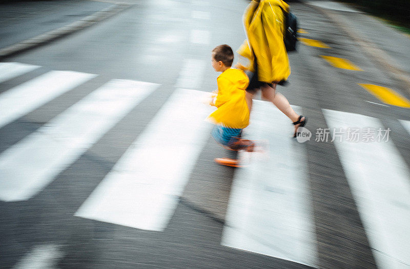 母亲和儿子穿着雨衣过马路，模糊的运动