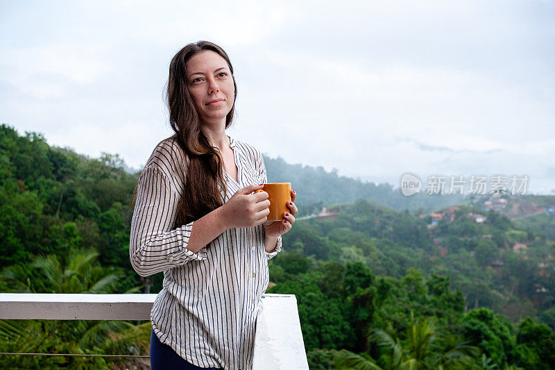 一名年轻女子在山顶上喝着茶，背景是全景