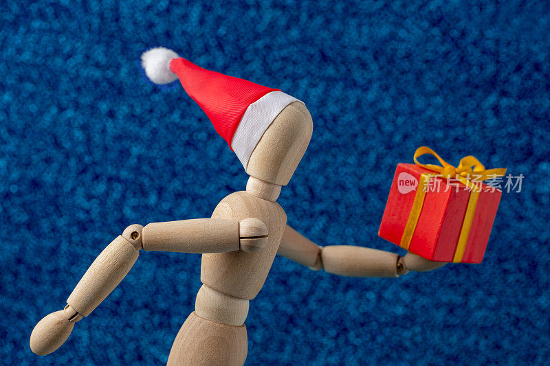 圣诞礼物-木制假人在圣诞老人的帽子拿着一个礼盒