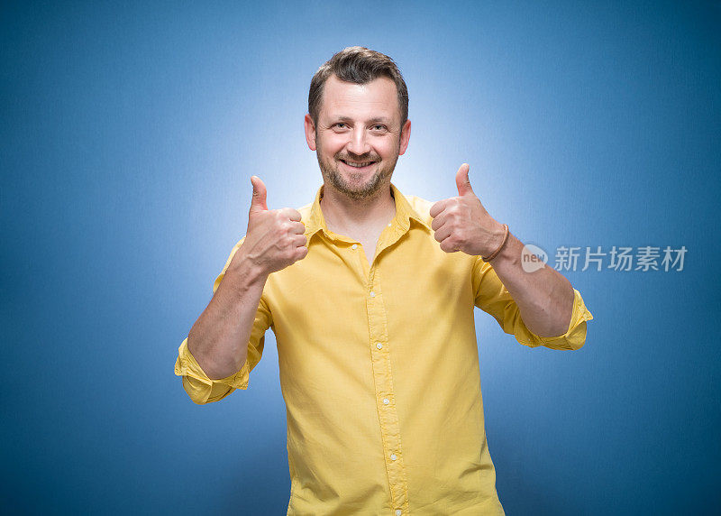 年轻男子竖起大拇指，喜欢概念蓝色背景，穿着黄色衬衫。是的，打手势，歌颂佳作