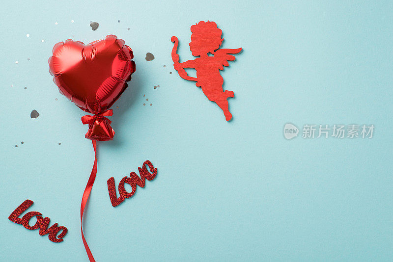 俯瞰照片的情人节装饰红色心形气球与丝带亮片彩纸题词爱和丘比特剪影孤立的淡蓝色背景与空白空间
