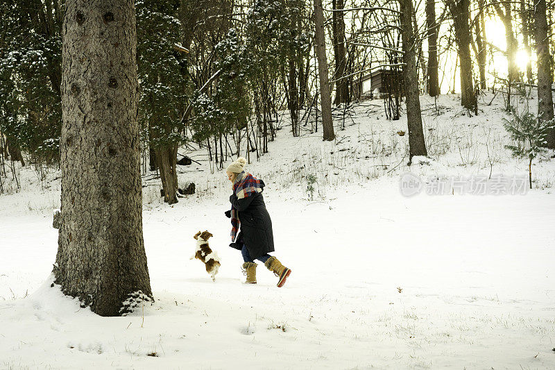 一名女子和她的查理骑士猎犬在雪地里嬉戏奔跑