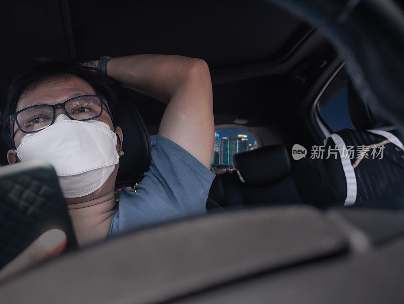 无聊的汽车司机等待在交通堵塞，年轻的亚洲男子戴着口罩使用手机，而在城市中驾驶。